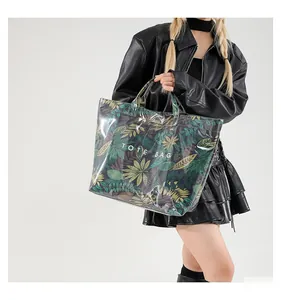 Détail du sac cabas en PVC transparent avec motif feuilles tropicales et texte blanc