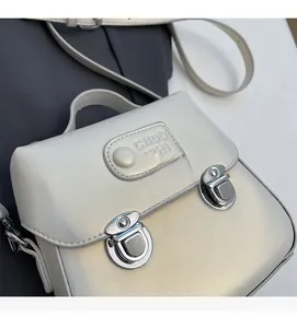 Détail du sac à bandoulière carré crème avec boucles métalliques et poignée