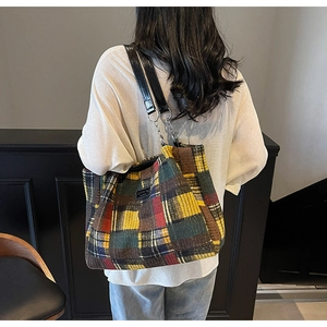 Detail of multi-color plaid tote bag with leather strap and chain accent on a model