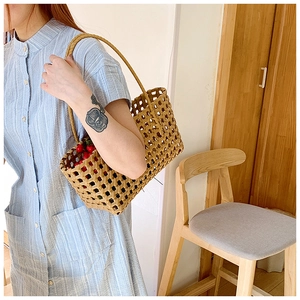 Close-up of light brown hollow woven tote bag held by model in striped blue dress