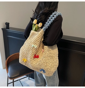 Detail of straw woven tote bag featuring colorful crochet bows and blue plush straps