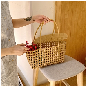 Detail of hollow woven straw tote bag with red berries on a wooden chair