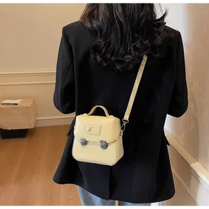 Détail d'un mini sac bandoulière jaune crème sur un blazer noir avec boutons argentés