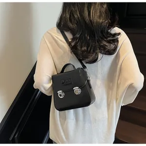 Petit sac à bandoulière carré noir en similicuir avec boucles argentées porté par un modèle