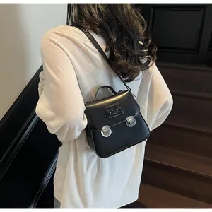 Détail d'un sac à main noir minimaliste avec deux boucles argentées et une poignée supérieure
