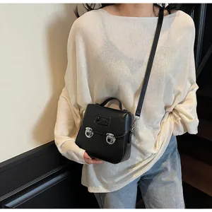 Détail du mini sac bandoulière noir avec boucles argentées et logo sur surface en cuir