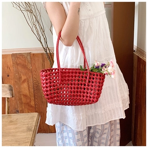 Close-up of a vibrant red woven basket bag held by a model in a rustic garden setting