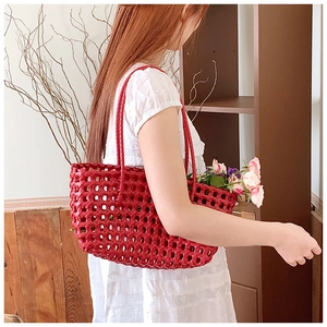 Detail of red hollow woven tote bag used as a floral basket with pink roses and dual handles