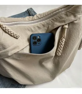 Detail view of a beige dumpling bag showing the front zipper pocket with a smartphone