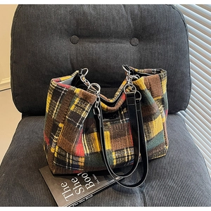 Detailed view of colorful checkered wool tote bag with black leather handles and metal chain