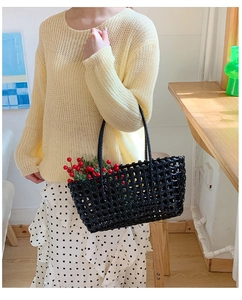 Close-up of a black woven hollow-out handbag styled with a yellow sweater and floral skirt