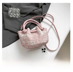Detail of pink woven bucket bag with knotted handles and crossbody strap on desk