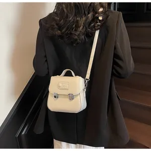 Gros plan du sac à bandoulière beige avec boucles argentées et rabat sur escalier bois