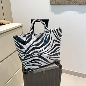 Grand sac cabas zébré élégant posé sur une valise grise pour les vacances