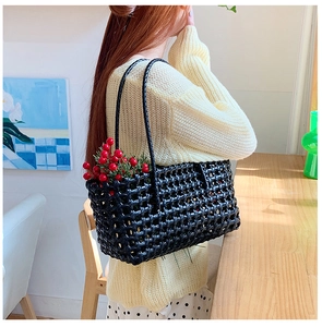 Detail of black woven straw tote bag with hollow mesh design and long slim handles