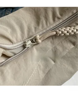 Detail of smooth metal zipper and woven pull rope on beige canvas dumpling bag