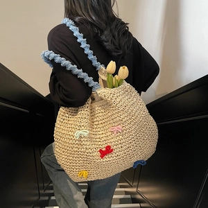 Handwoven straw tote bag with colorful crochet bows and blue pleated shoulder strap
