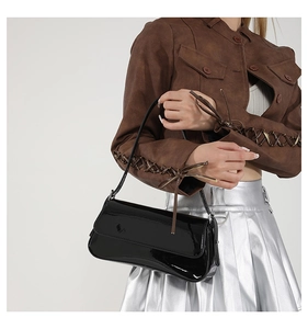 Close-up of a black patent leather baguette bag with a glossy finish and shoulder strap