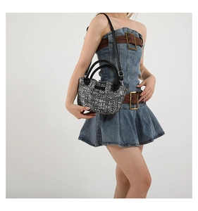 Detail view of woven pattern handbag with black dual handles and adjustable shoulder strap