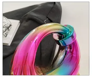 Detail of the ergonomic round handle and rainbow gradient metallic finish clutch bag