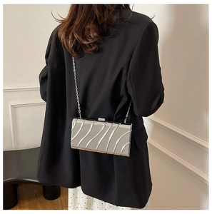 Detail of silver metallic clutch with wavy texture and detachable chain strap on black blazer