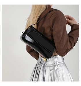 Detail of a black patent leather shoulder bag with a shiny finish and gold zipper
