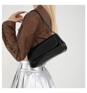 Side view of black patent leather underarm bag paired with brown suede jacket and skirt