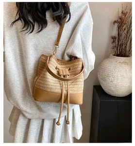 Detailed view of woven straw bucket bag with brown leather strap worn by a model