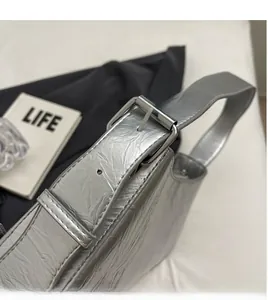 Detail of adjustable silver metal buckle and shiny crinkled leather strap on the bag