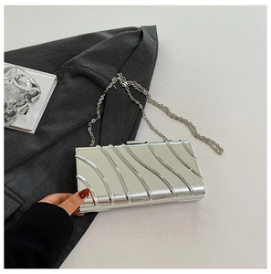 Dettaglio della clutch argento metallizzato con texture a onde e catenina su blazer