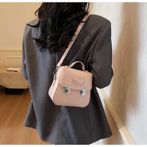 Sac bandoulière rose minimaliste avec fermoir rotatif porté sur un costume gris