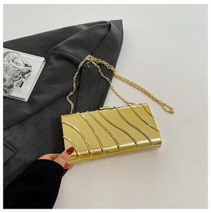 Dettaglio della borsa clutch in acrilico dorato con trama a onde e catena sottile