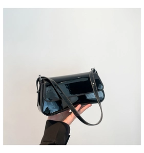 Close-up of a minimalist black patent leather shoulder bag held against a white wall