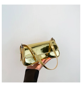 Close-up of golden mirror finish patent leather baguette bag held in hand