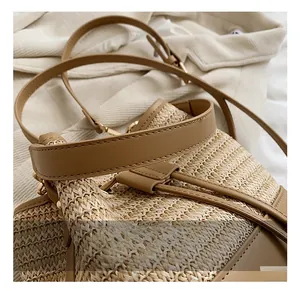 Detail of hand-woven straw bucket bag with dark brown leather handle and drawstring