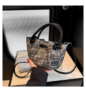 Detail of woven bucket bag featuring knotted black leather handles and long shoulder strap