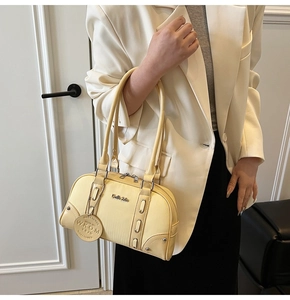 Close-up of cream Boston bag with metal logo and tag detail on model in white suit