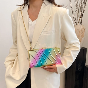 Clutch in acrilico lucido sfumato con catena dorata indossata da una modella in abito bianco