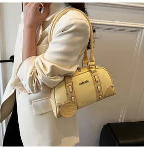 Close-up of yellow Boston bag detail featuring metal logo and hanging leather tag