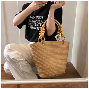 Detail of hand-woven straw tote bag featuring decorative wooden beads on the handle