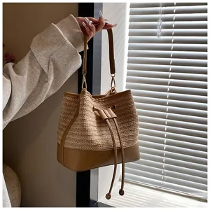 Close-up of woven straw bucket bag with camel synthetic leather handles and drawstring