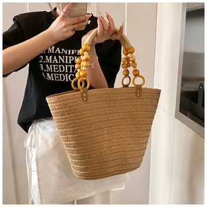 Detail of straw woven bucket bag featuring decorative yellow wooden bead handle
