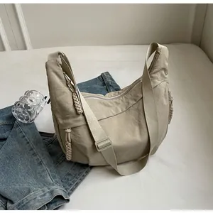 Detail of beige nylon hobo bag with braided zipper pull on a minimalist background