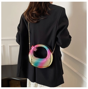 Detail of an iridescent asymmetric acrylic handbag with a gold chain on a black blazer