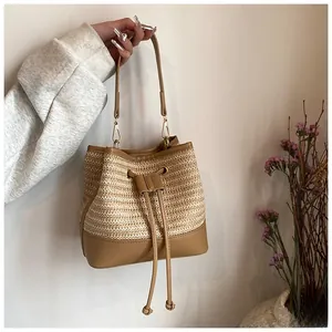 Detail of hand-woven straw bucket bag with brown leather trim and tassel drawstrings