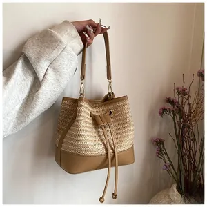 Detail of straw bucket bag featuring cream weaving, brown leather base and drawstring