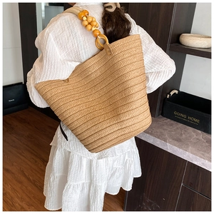 Detail of hand-woven straw bucket bag with large natural wood bead shoulder strap