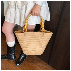 Detail of straw tote bag showing wooden rings and beaded handle on natural woven fabric
