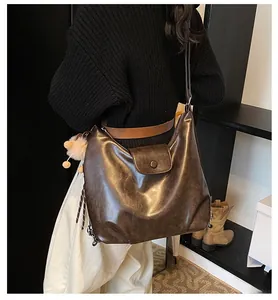 Close-up of vintage brown hobo bag with wax texture and fluffy ball charm on model