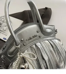 Detail of silver pleated handbag with pearl charms and heart pendant on a metallic PU leather